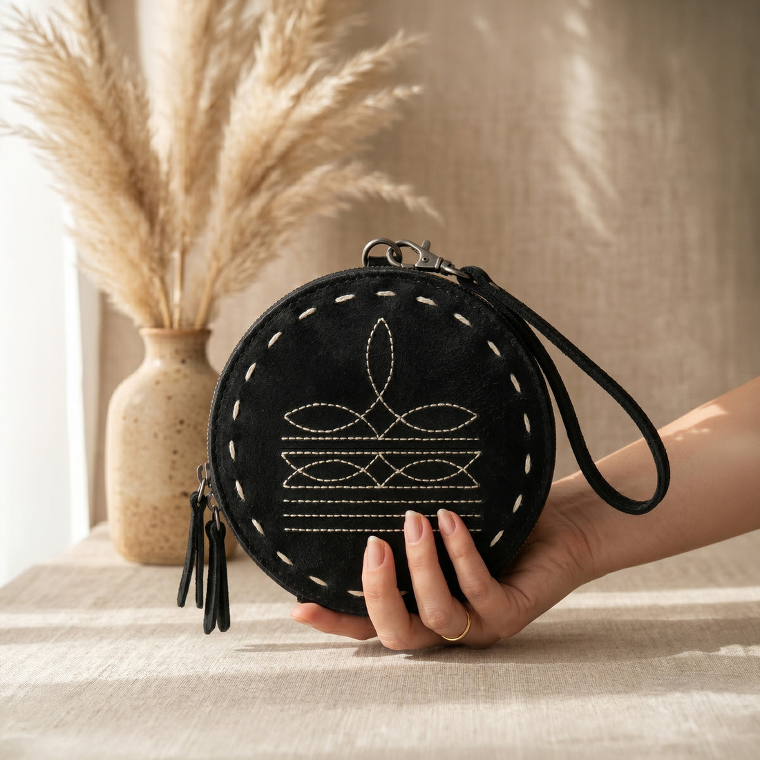 Hand holding black western leather round wristlet wallet